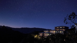 A two-story house with multiple windows and a balcony, surrounded by trees and hills under a starry night sky. - Villa Ryusei (Shima)