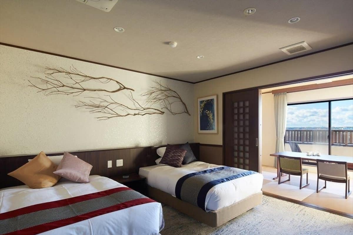 A hotel room with two beds, a dining table, and a view of the city.