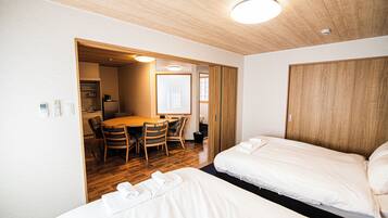 Hotellihuone, jossa on kaksi sänkyä, ruokailutila pöydän ja tuolien kera sekä puinen katto.
