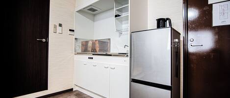 A compact kitchen with a stainless steel refrigerator, white cabinetry, and a wooden floor.