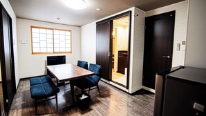 Un comedor moderno con una mesa de madera y sillas tapizadas en azul, una puerta corrediza que da a una cocina y un refrigerador negro.