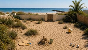 Una playa arenosa con una valla de madera, una palmera y un balón de playa.