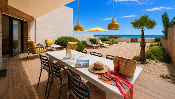 Un espacio exterior para comer con vista a la playa, una mesa con sillas y una sombrilla.