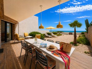 An outdoor dining area with a view of the beach, a table with chairs, and a sun umbrella. - Carnon Beach Sand : The Beach as Your Garden (Mauguio)
