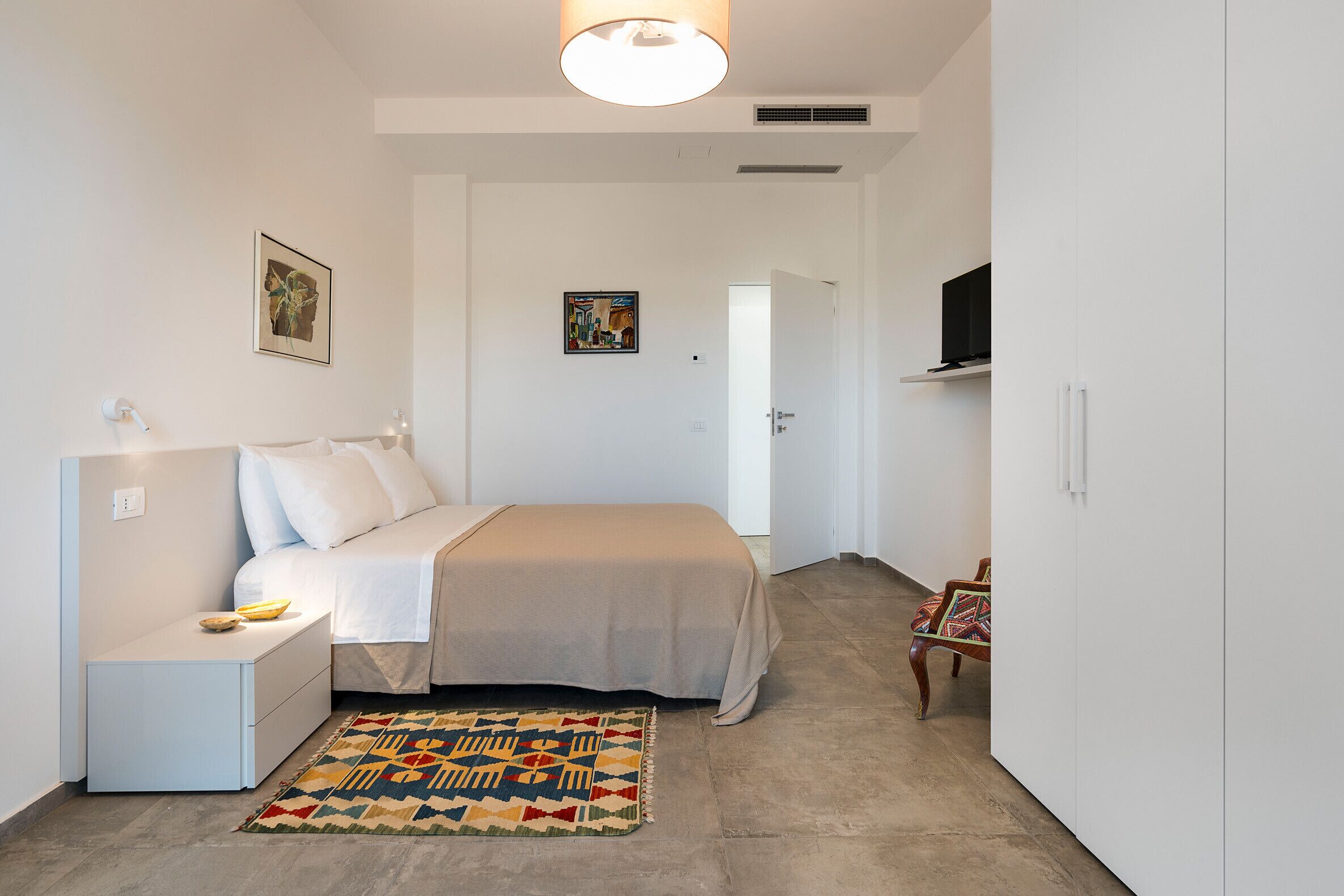 A bedroom with a bed, nightstand, lamp, and a colorful rug.