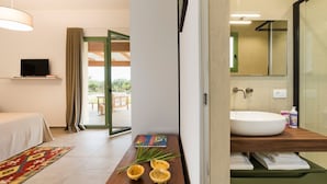 A modern hotel room with a bed, a TV, a wooden side table with a book and decorative items, a large window with curtains, and a bathroom with a sink and mirror. - Beautiful villa with pool in Menfi (Menfi)