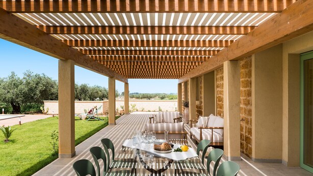 An outdoor dining area with a wooden pergola, a table set with plates and glasses, and a sofa with cushions. - Beautiful villa with pool in Menfi (Menfi)