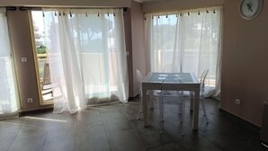 Une pièce avec une table à manger dont le plateau est en verre, des rideaux transparents et une horloge au mur.