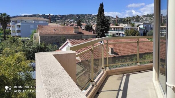 Un balcon donnant sur un quartier résidentiel, avec des maisons aux toits recouverts de tuiles rouges et une colline en arrière-plan.