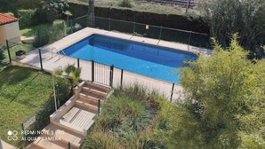 Une piscine rectangulaire entourée d’une cl ôture, avec une terrasse en bois et une zone herbeuse agrémentée d’arbustes.