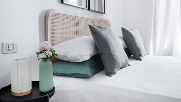 A neatly arranged bedroom with a bed, pillows, a vase with flowers, and a bedside table with a lamp.