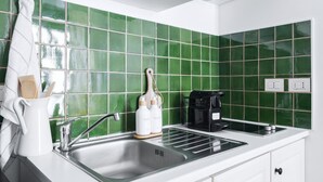 A modern kitchen with green tiles, a stainless steel sink, and a coffee maker.