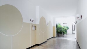A hallway with a tiled floor and walls painted in a light beige color. There are large circular wall decorations and wall-mounted light fixtures.