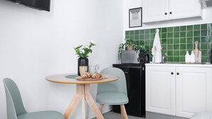A modern kitchen with white cabinets, a green tiled backsplash, a black dishwasher, and a round wooden table with two chairs.