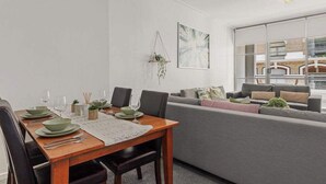 A modern living room with a dining area, a grey sofa, and a large window offering a view of the city.