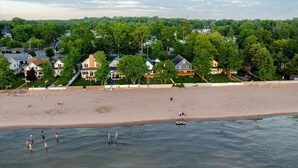 A beach with houses in the background and people swimming in the water. - Parks  Slice Heaven | 2BR Waterfront| with Hot tub (Sylvan Beach)