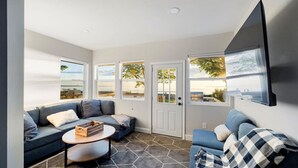 A modern living room with a gray sofa, a round coffee table, and a large TV mounted on the wall. - Parks  Slice Heaven | 2BR Waterfront| with Hot tub (Sylvan Beach)