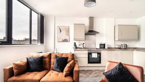 Una sala de estar moderna con sofá y sillón, una cocina equipada y un ventanal con vistas a edificios.
