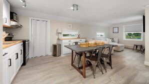 A modern kitchen with white cabinets, a dining table with chairs, a microwave, and a trash can. - "Whitewater-The Genoa" on Oneida Lake/Sleeps 8! (Canastota)