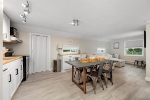 A modern kitchen with white cabinets, a dining table with chairs, a microwave, and a trash can.