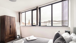 A hotel room with a large window, a wardrobe, a bed with pillows, and a bedside table. - Fabulous 1 BED Apartment Central Wrexham with WiFi (Wrexham)