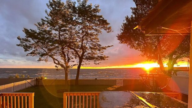 A deck with wooden railings, a bench, and a trash can. - Park Peaks on the Beach| 4BR Waterfront | Hot tub | Sleeps 12! (Sylvan Beach)