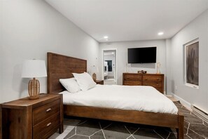 Un dormitorio con cama de madera, mesita de noche, cómoda, televisor y un cuadro en la pared.
