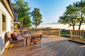 Una terraza de madera con mobiliario exterior, una parrilla y vista al agua.