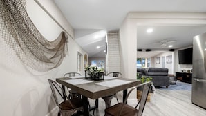 A modern dining area with a wooden table and metal chairs, a white brick wall, and a hanging net decoration. - Park Peaks on the Beach| 4BR Waterfront | Hot tub | Sleeps 12! (Sylvan Beach)