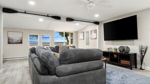 A living room with a gray sectional sofa, a flat-screen TV mounted on the wall, and a ceiling fan. - Park Peaks on the Beach| 4BR Waterfront | Hot tub | Sleeps 12! (Sylvan Beach)