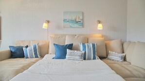 Une chambre d’hôtel avec un grand lit, plusieurs oreillers, un tableau représentant des voiliers et deux lampes fixées au mur.