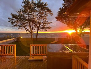 A wooden deck with a bench, a trash can, and a view of the ocean at sunset.