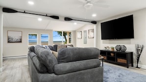 Un soggiorno con un divano ad angolo grigio, una TV a schermo piatto montata a parete e una ventola a soffitto.