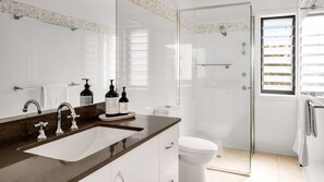 Ein modernes Badezimmer mit einem großen Spiegel, einem Waschbecken mit zwei Wasserhähnen, einer Toilette und einer Duschkabine.