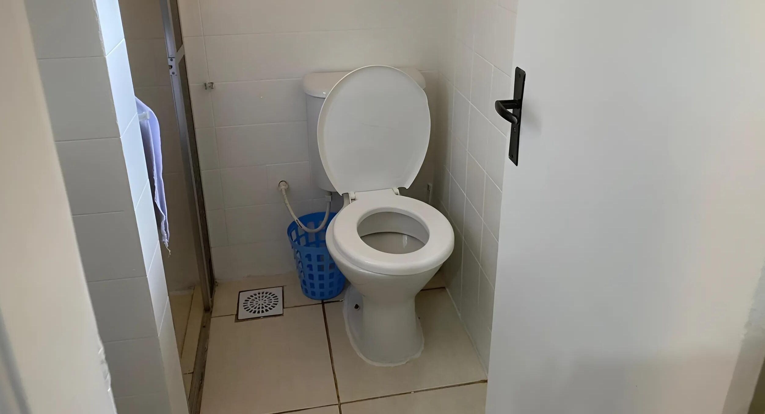 Um banheiro com vaso sanitário branco, lixeira azul e pia branca.