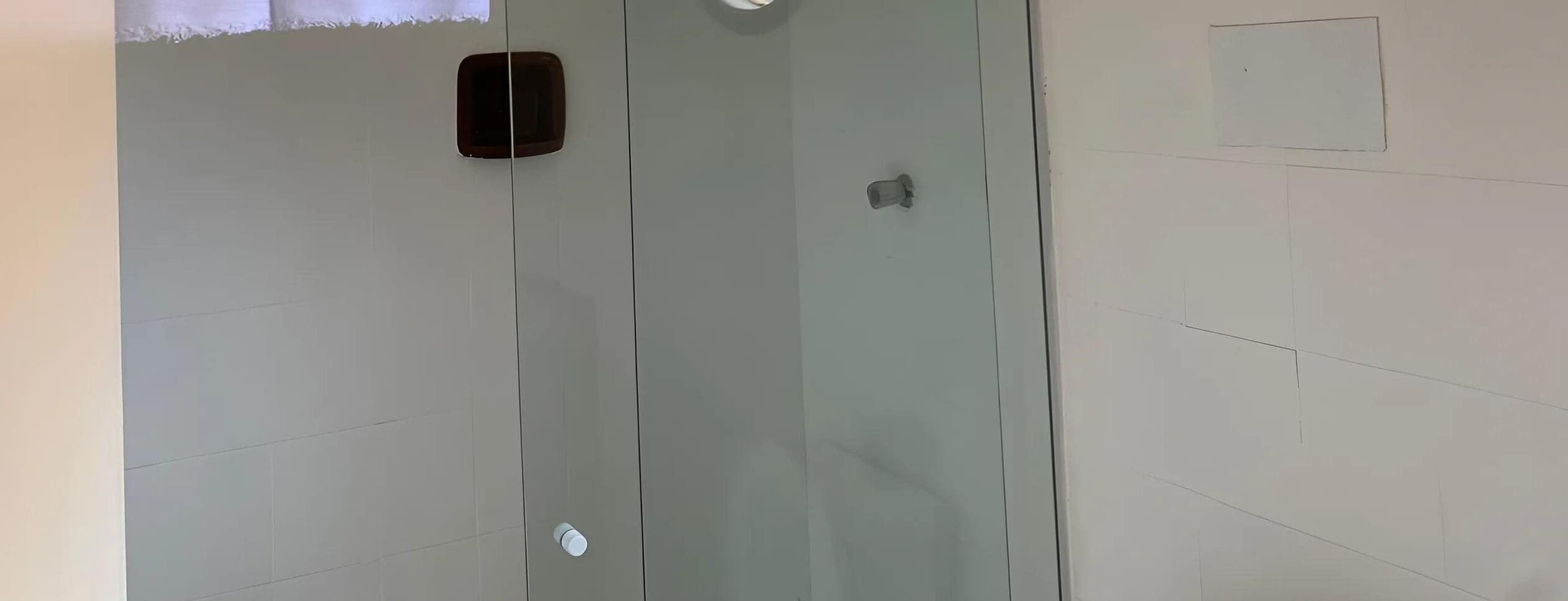 Een badkamer met een glazen douchecabine en een zeepdispenser bevestigd aan de muur.