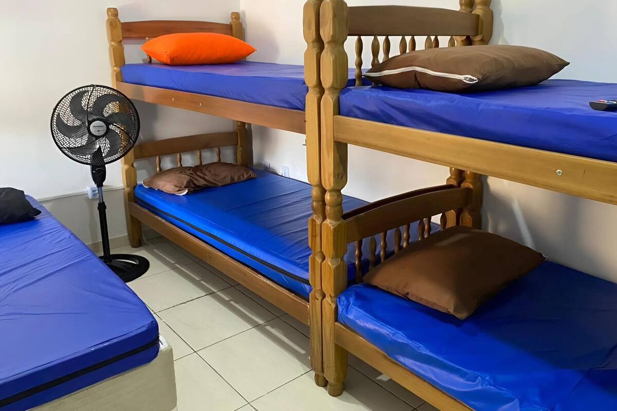 Een slaapkamer met een stapelbed, blauw beddengoed, een ventilator en kussens.