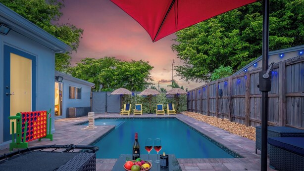 Zona de piscina con sillas de descanso, una mesa con bebidas y una sombrilla roja.