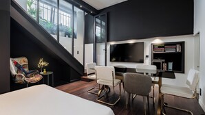 A modern hotel room with a large bed, a desk with a flat-screen TV, and a staircase leading to a balcony with plants. - Contemporary Excellence, by Veeve (Paris)