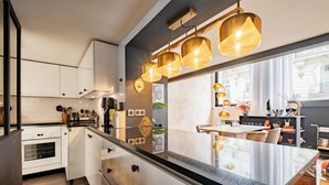 A modern kitchen with white cabinetry, a black countertop, and pendant lighting. - Contemporary Excellence, by Veeve (Paris)