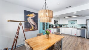 A modern kitchen with white cabinets, stainless steel appliances, and a wooden dining table with wicker chairs. - Oceanfront Condo | Couples | Cozy (Port St. Joe)