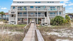 A multi-story beachfront building with a wooden walkway leading to the entrance, multiple balconies, and a view of the beach. - Oceanfront Condo | Couples | Cozy (Port St. Joe)