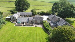 An aerial view of a rural property with stone buildings, a large lawn, and surrounding fields. - Bolehill Farm Cottages (Bakewell)