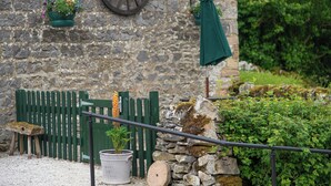 A rustic stone building with a wooden wheel, potted plants, a bench, and a metal railing. - Bolehill Farm Cottages (Bakewell)