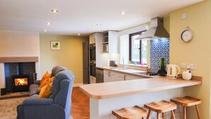 A modern kitchen with a central island, a built-in stove, and a dining area with a sofa and bar stools. - Bolehill Farm Cottages (Bakewell)