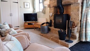 A cozy living room with a stone fireplace, a television, and a comfortable sofa. - Bolehill Farm Cottages (Bakewell)