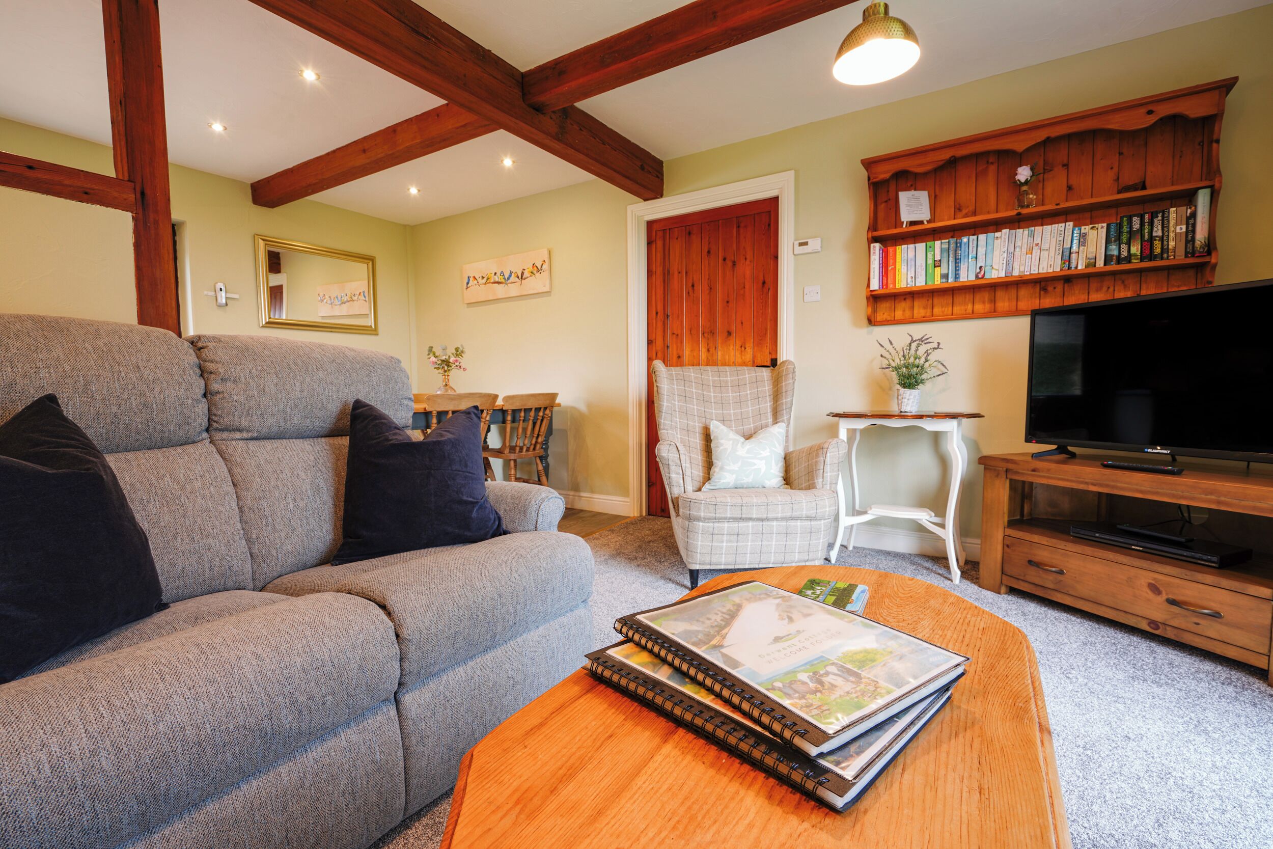 A living room with a sofa, armchair, coffee table, bookshelf, and television.
