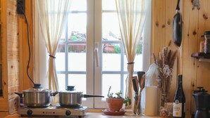 Una cocina de madera con dos estufas a gas, un fregadero y una ventana con cortinas. Hay ollas, sartenes y una botella en la encimera.