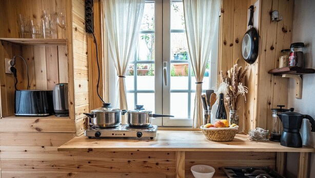 Una cocina de madera con estufa, ollas y una ventana con cortinas.