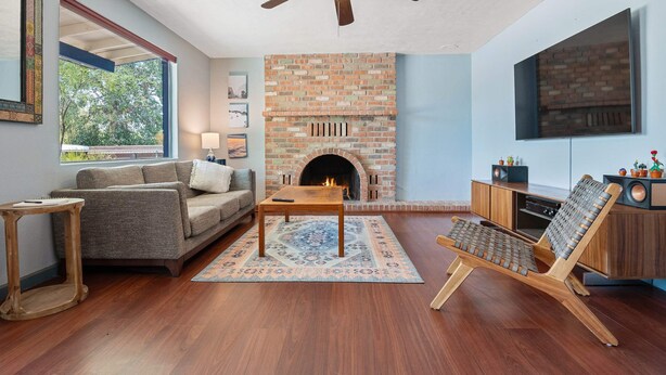 A living room with a brick fireplace, a ceiling fan, a sofa, a coffee table, and a TV mounted on the wall. - Sonoran Velo Summary: (Tucson)